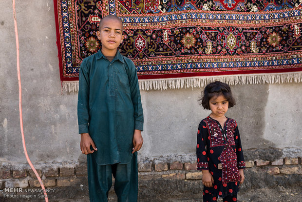 دو کودک پای دیوار با فرشی که روی دیوار برای خشک شدن انداخته شده است.( روستایی نزدیک زابل)