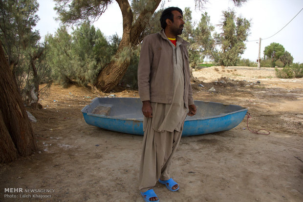 یک صیاد تالاب هامون ایستاده کنار قایق و منطقه خشک زابل استان سیستان و بلوچستان