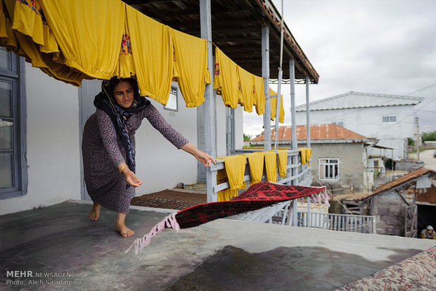 مهری در حال پهن کردن قالیچه دست بافتش در ایوان خانه خود می باشد. لباسهای دوخته و شسته شده در ایوان برای خشک شدن پهن شده اند.