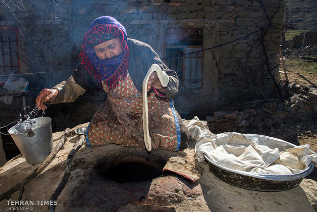 A Turkmen woman in traditional dress bakes bread in a tandoor in her house. Although the village has a bakery, most of women prefer to bake bread in their houses.