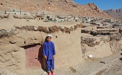 A boy stands by a tiny house in Makhunik