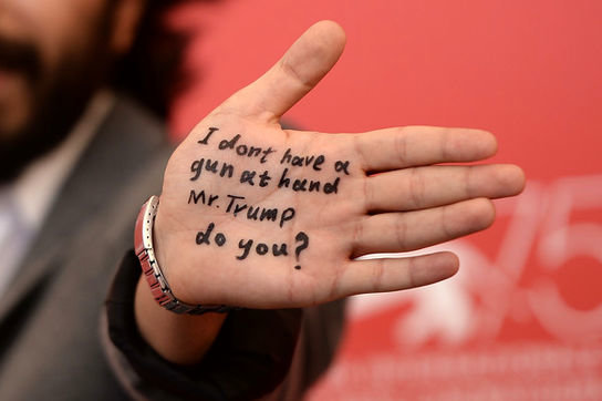 Iranian actor Vahid Raad shows his palm bearing an inscription reading, “I don’t have a gun at my hand Mr. Trump, do you?” during a photocall for his latest movie “As I Lay Dying” at the 75th Venice I