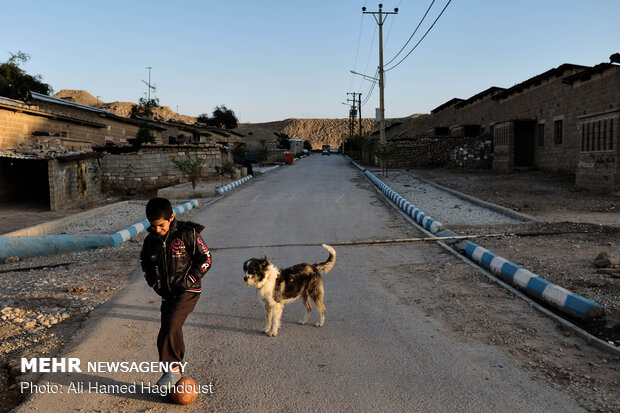 محمد چالنگ 10 ساله کنار سگ خود در یکی از محلات روستای نفت سفید در حال توپ بازی است.