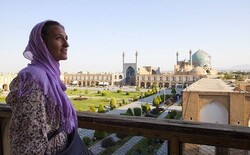 A foreign traveler poses for a photo while standing at the terrace of the 17th-century Ali-Qapu Palace, a top masterpiece of Iranian architecture, which punctuates the middle of two-story arcades encircling the enormous Imam Square; a UNESCO-registered site in Isfahan, central Iran.