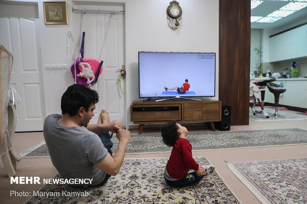 پدر و فرزندی در حال ورزش در خانه با برنامه ورزشی اینترنتی  هستند