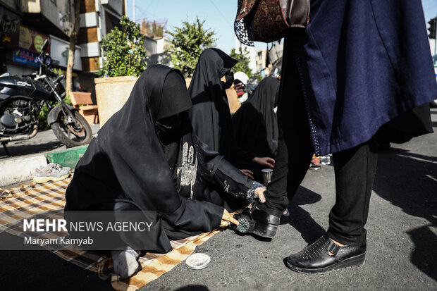 زنان در حال واکس زدن کفش زنان شرکت کننده در مراسم راهپیمایی اربعین حسینی در تهران هستند