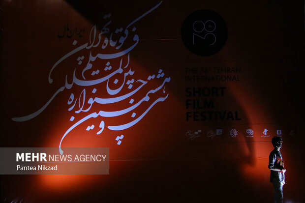 یکی از حاضرین در جشنواره فیلم کوتاه هران در حال گرفن عکس یادگاری با بنرهای جشنواره فیلم کوتاه تهران است