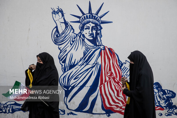 دو دآنش آموز حاضر در مراسم یوم الله ۱۳ آبان در تهران در حال عبور از مقابل نقاشی مجسمه آزادی که بر روی دیوار لانه جاسوسی امریکا نقش بسته هستند