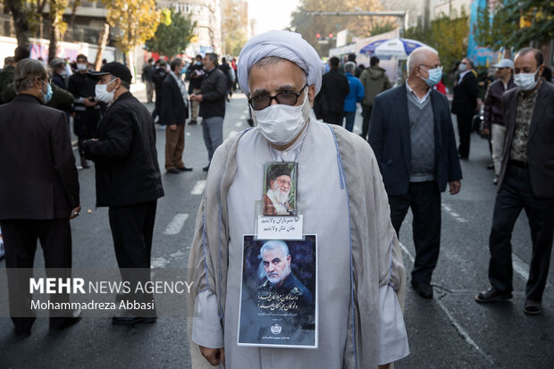 یک روحانی در مراسم یوم الله ۱۳ آبان در تهران عکس مقام معظم رهبری و شهید حاج قاسم سلیمانی را بر روی سینه خود نصب کرده است