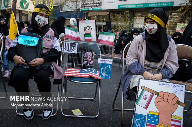 دو دانش آموز حاضر در مراسم یوم الله ۱۳ آبان در تهران بصورت نمادین  آدمک جو بایدن رئیس جمهور آمریکا را در قفس همراه خود دارند