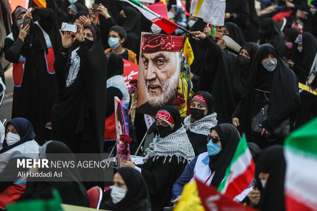 عکس شهید حاج قاسم سلیمانی در دست یکی از شرکت کنندگان زینت بخش مراسم راهپیمایی است