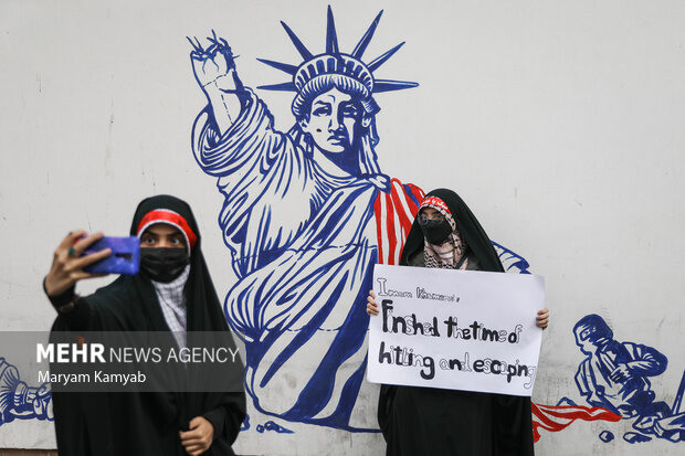 دو دانش آموز حاضر در مراسم یوم الله ۱۳ آبان در تهران در حال گرفتن عکس با نقاشی مجسمه آزادی که بر روی دیوار لانه جاسوسی امریکا نقش بسته است، هستند