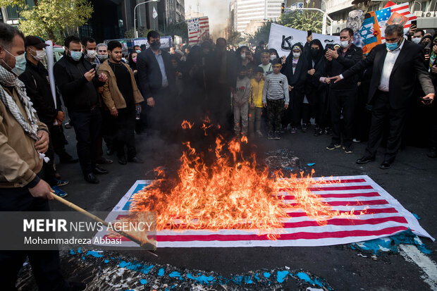 شرکت کنندگان در مراسم یوم الله ۱۳ آبان در تهران در حال آتش زدن پرچم آمریکا هستند