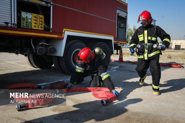شرکت کنندگان مسابقه در حال بستن شیلنگ به مخزن  ماشین مخصوص حمل آب آتش نشانی هستند