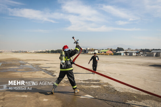 شرکت کننده مسابقات ورزشی آتش نشانان نیروی هوایی ارتش برای انجام مسابقه شیلنگ آب ماشین آتش نشانی را بررسی می کند