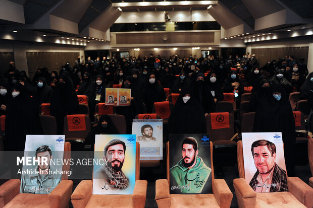 حاضرین در حال ادای احترام به سرود جمهوری اسلامی ایران در مراسم آیین تجلیل از مادران و همسران شهدا هستند