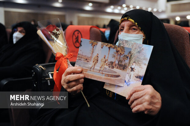 یکی از ماداران شهدا تصویر فرزند شهیدش را در آیین تجلیل از مادران و همسران شهدا در دست دارد
