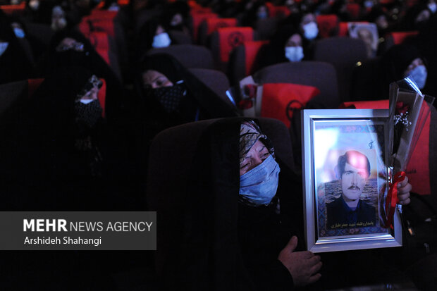 یکی از ماداران شهدا تصویر فرزند شهیدش را در آیین تجلیل از مادران و همسران شهدا در دست دارد