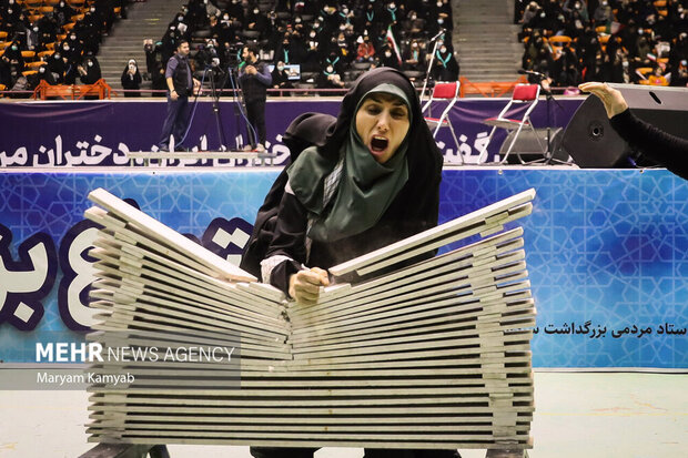 یک بانوی رزمی کار در حال زدن ضربه جهت شکستن اجسام سخت در همایش دختران حاج قاسم در سالن ۱۲ هزار نفری مجموعه ورزشی آزادی تهران است