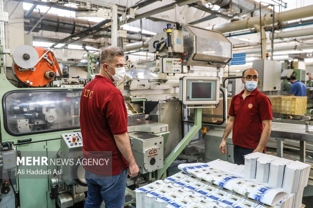کارگران شرکت دخانیات در حال قرا دادن پاکت های کاغذی سیگار در دستگاه هستند