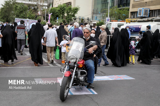 خانواده ای سوار بر موتور سیکلت در مراسم راهپیمایی روز جهانی <a href='https://sayeb.ir/tag/%d9%82%d8%af%d8%b3'>قدس</a> در میدان فلسطین از روی پرچم آمریکا و رژیم صهیونیستی عبور می کند