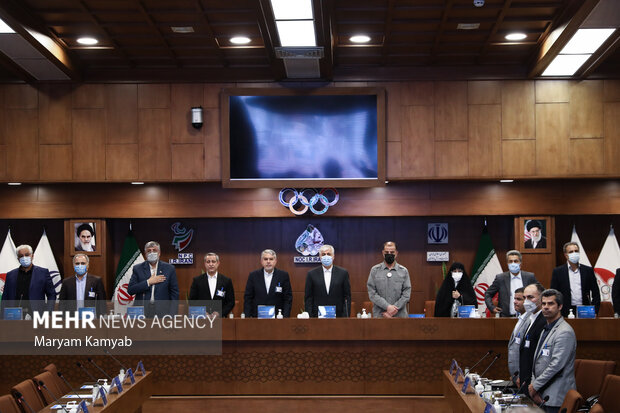رئیس و اعضای مجمع کمیته ملی المپیک در حال ادای احترام به سرود جمهوری اسلامی ایران در ابتدای مراسم هستند