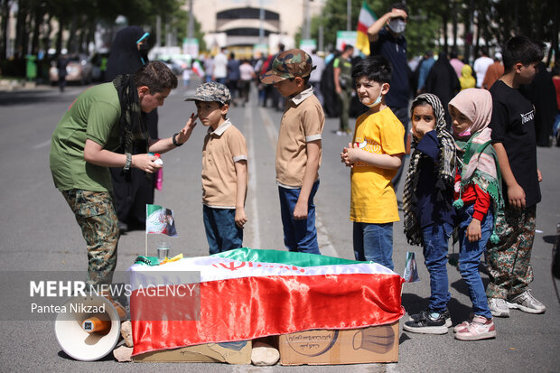 یکی از نوجوانان در حال کشیدن پرچم بر روی صورت کودکان در محوطه ورزشگاه آزادی است