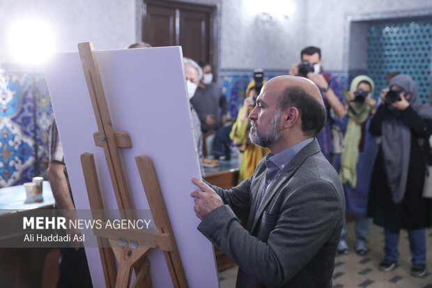 حمید فروتن در نشست خبری ششمین دوره نشان سال عکس مطبوعاتی ایران در حال امضا بر پوستر این دوره جشنواره است 