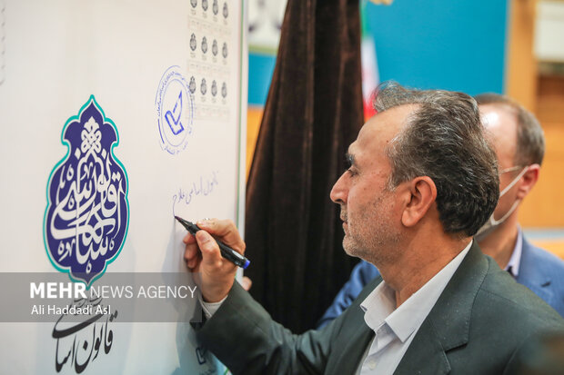 محمد دهقان معاون حقوقی رئیس جمهور در حال ثبت یادگاری بر تمبر رونمایی شده در همایش ملی مسئولیت اجرای قانون اساسی است