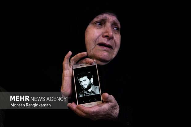 مادر شهید یونس یوسف‌زاده عکس فرزند شهیدش را مراسم وداع با پیکر شهید در معراج شهدا در دست دارد