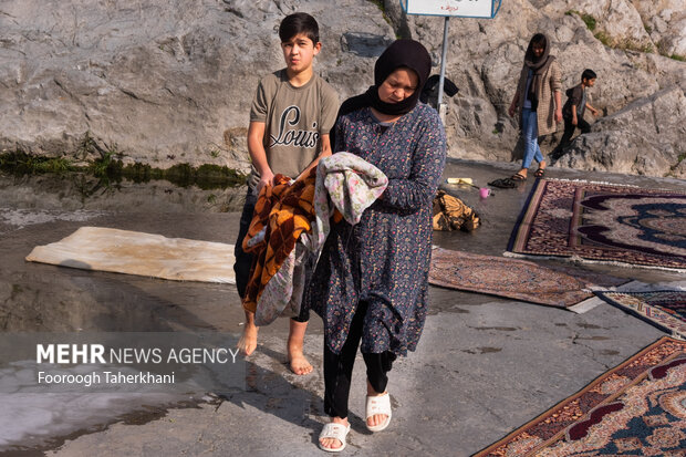 خانواده ای در چشمه علی بعد از شستن فرش برای کشیده شدن آب آن را آماده می کنند