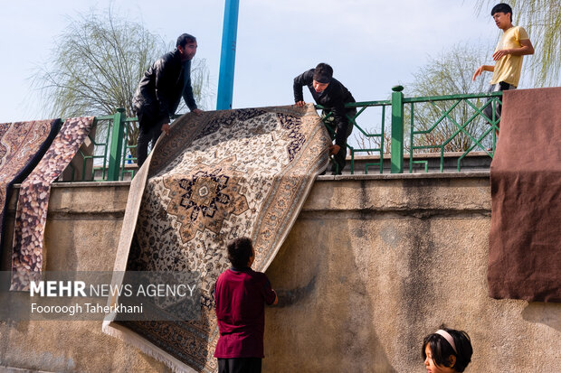 خانواده ای هل ری بعد شستن فرش خود در چشمه علی آن را برای کشیده شدن آب روی نرده ها می اویزد