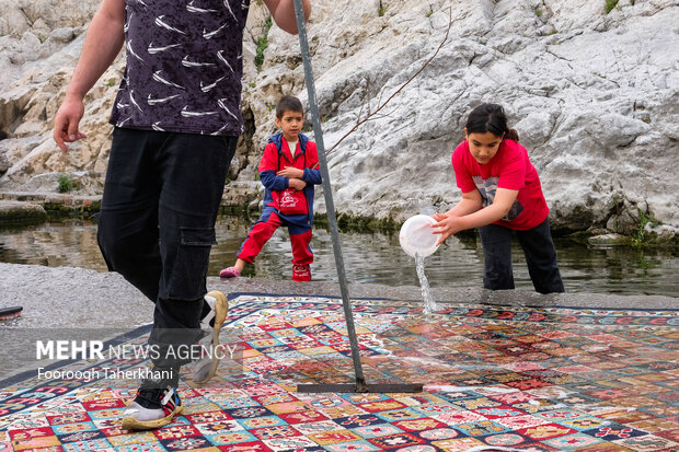خانواده ای همراه با فرزندان خود در چشمه علی فرش خود را شست شو می دهند