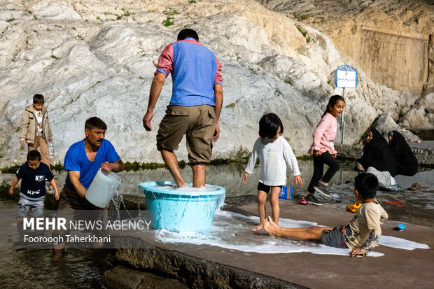 خانواده ای همراه با فرزندان خود بعد از تاریک شدن هوا در چشمه علی فرش خود را شست شو می دهند