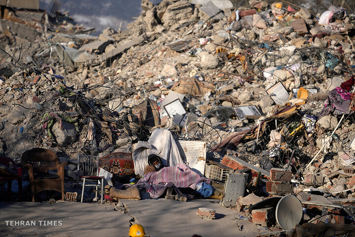 A man sleeps in front of a destroyed building in Kahramanmaras, southeastern Turkey, on February 13. Thousands, left homeless by a massive earthquake that struck Turkey and Syria, packed into crowded tents or lined up in the streets for hot meals, while the desperate search for anyone still alive likely entered its last hours. [Khalil Hamra/AP Photo]