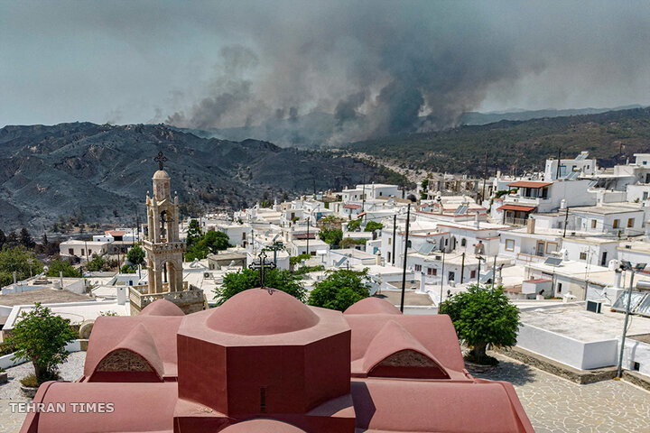 A view of the village of Asklipieio, as a wildfire burns in the background, on the island of Rhodes, Greece, on July 26. [Nicolas Economou/Reuters]
