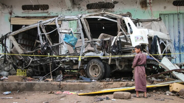 A child stands next to a Yemeni school bus that exploded in the Saudi airstrike on Dahyan on Aug. 9, 2018, killing 40 schoolchildren